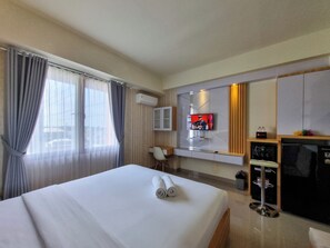 A hotel room with a bed, a desk, a TV, and a minibar. - Best Place And Cozy Studio At Altuz Seturan Yogyakarta Apartment (Depok)