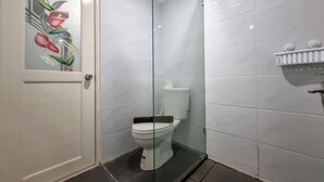 Ein Badezimmer mit Duschkabine aus Glas, Toilette und weiß gefliesten Wänden.