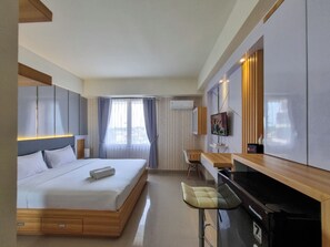 A modern hotel room with a large bed, a desk, a chair, a television, and a window with curtains. - Best Place And Cozy Studio At Altuz Seturan Yogyakarta Apartment (Depok)