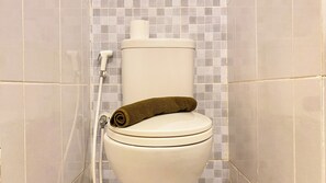 Un inodoro con una toalla enrollada en el asiento, un tirador de la cisterna blanco y un cabezal de ducha adherido a la pared.