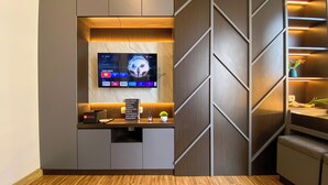 Et moderne opholdsområde med et fladskærms-tv på væggen, et lille bord med bakke og en dekorativ plante.