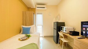 A hotel room with a bed, a desk with a microwave, a refrigerator, a chair, and a TV. - Minimalist And Compact Studio (No Kitchen) At Apartment B Residence (Pagedangan)