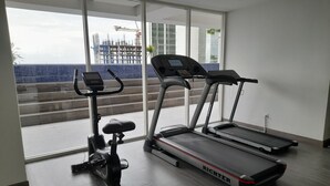Une salle de sport moderne équipée de deux tapis de course et d’un appareil elliptique, de grandes fenêtres donnant sur un chantier de construction, et présentant un design épuré et minimaliste.