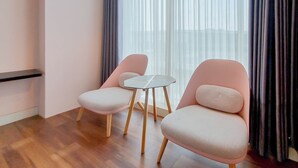Une pièce moderne avec deux fauteuils roses et une petite table, un plancher en bois et une fenêtre ornée de rideaux légers.