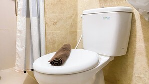 Toilette mit Handtuch auf dem Sitz, an der Wand befestigtem Toilettenpapierhalter und einer Duschvorhang.