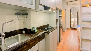 A compact kitchen with a sink, stove, and cabinets. - Cozy Studio Apartment At Transpark Cibubur (Depok)