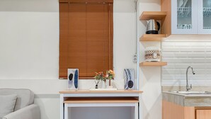 A compact kitchen with a wooden countertop, two stools, a sink, and a window with blinds. - Comfort 2Br At Meikarta Apartment Cikarang (Cikarang)