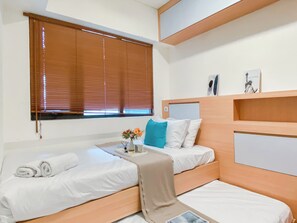 Une chambre d’hôtel avec deux lits simples, une petite table ornée d’un vase de fleurs et une fenêtre avec des stores.