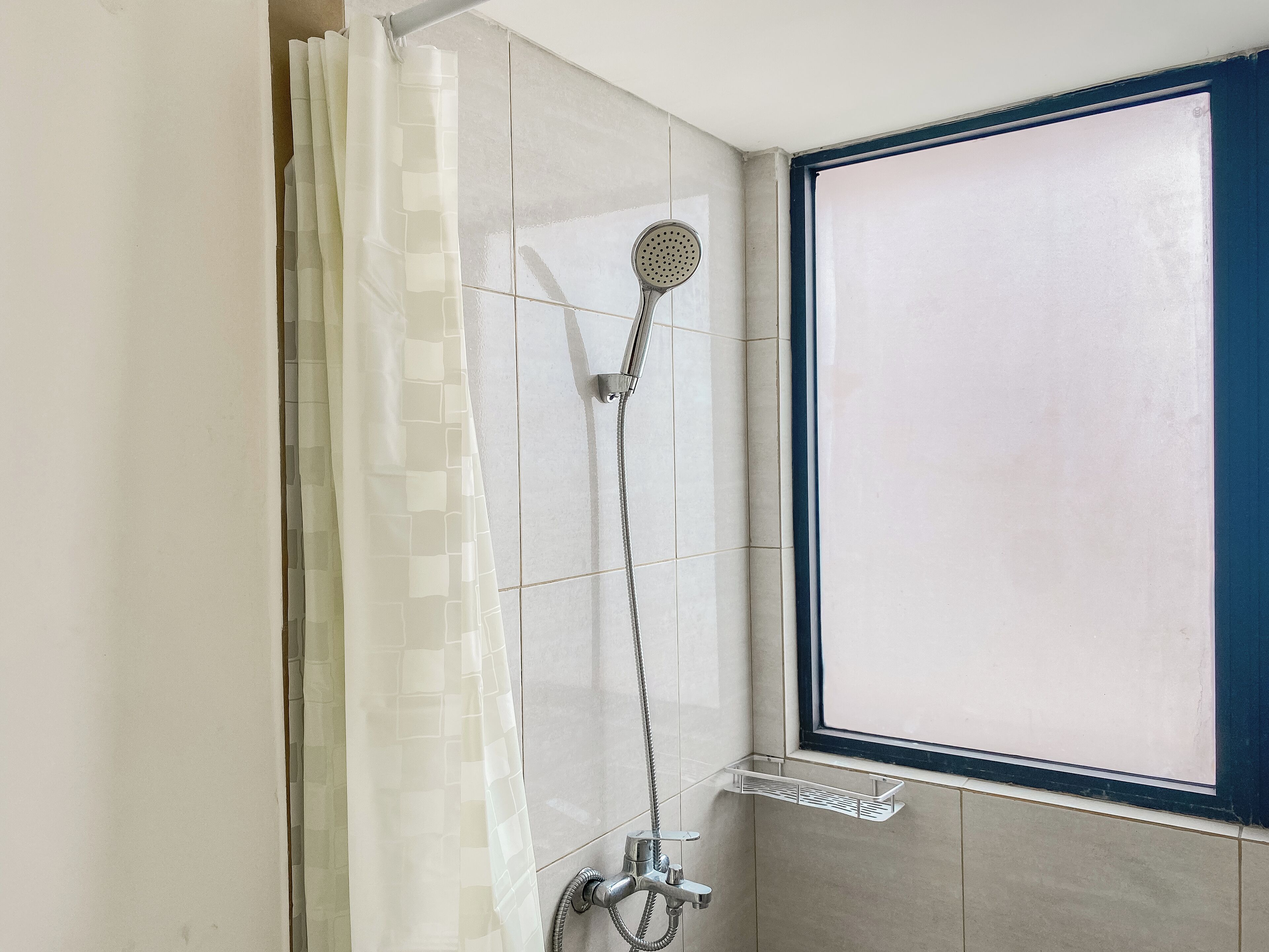 A shower with a handheld showerhead, a wall-mounted faucet, and a window with a blue frame.