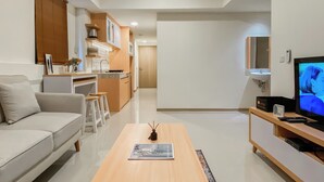 A modern living room with a sofa, coffee table, and TV. A kitchen is visible in the background with a dining area. - Comfort 2Br At Meikarta Apartment Cikarang (Cikarang)