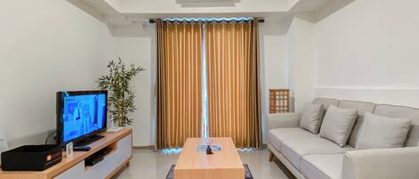 Una sala de estar moderna con un televisor de pantalla plana, una mesa de centro de madera, un sofá color beige y un ventanal con cortinas.
