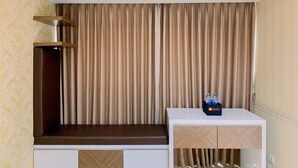 A hotel room with a minibar, an air conditioning unit, and a curtain backdrop.