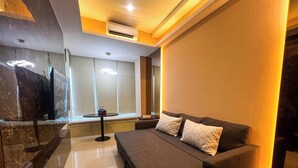 A modern hotel room with a large bed, a flat-screen TV, a small table with a water bottle, and a large window. - Well Furnished 1Br At Anderson Supermall Mansion Apartment (Surabaya)