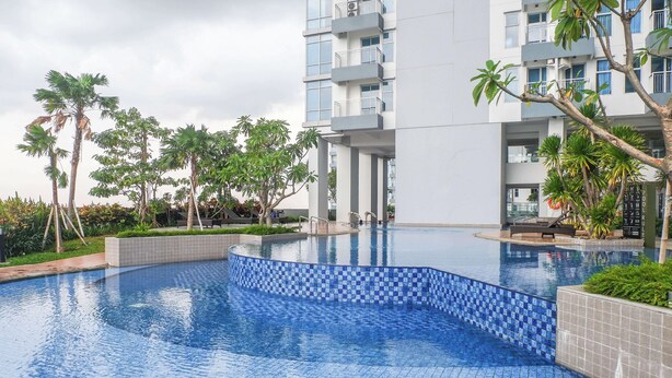 A swimming pool with tiled edges, surrounded by palm trees and a modern building with balconies. - Well Furnished 1Br At Anderson Supermall Mansion Apartment (Surabaya)