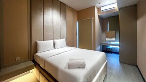 A modern hotel room with a large bed, a small desk, and a bathroom visible through an open door. - Well Furnished 1Br At Anderson Supermall Mansion Apartment (Surabaya)