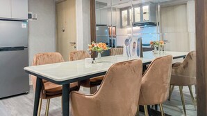 A modern dining area with a glass table, six cushioned chairs, and a kitchen in the background. - Homey And Modern Look 3Br At Meikarta With Balcon Apartment (Cikarang)