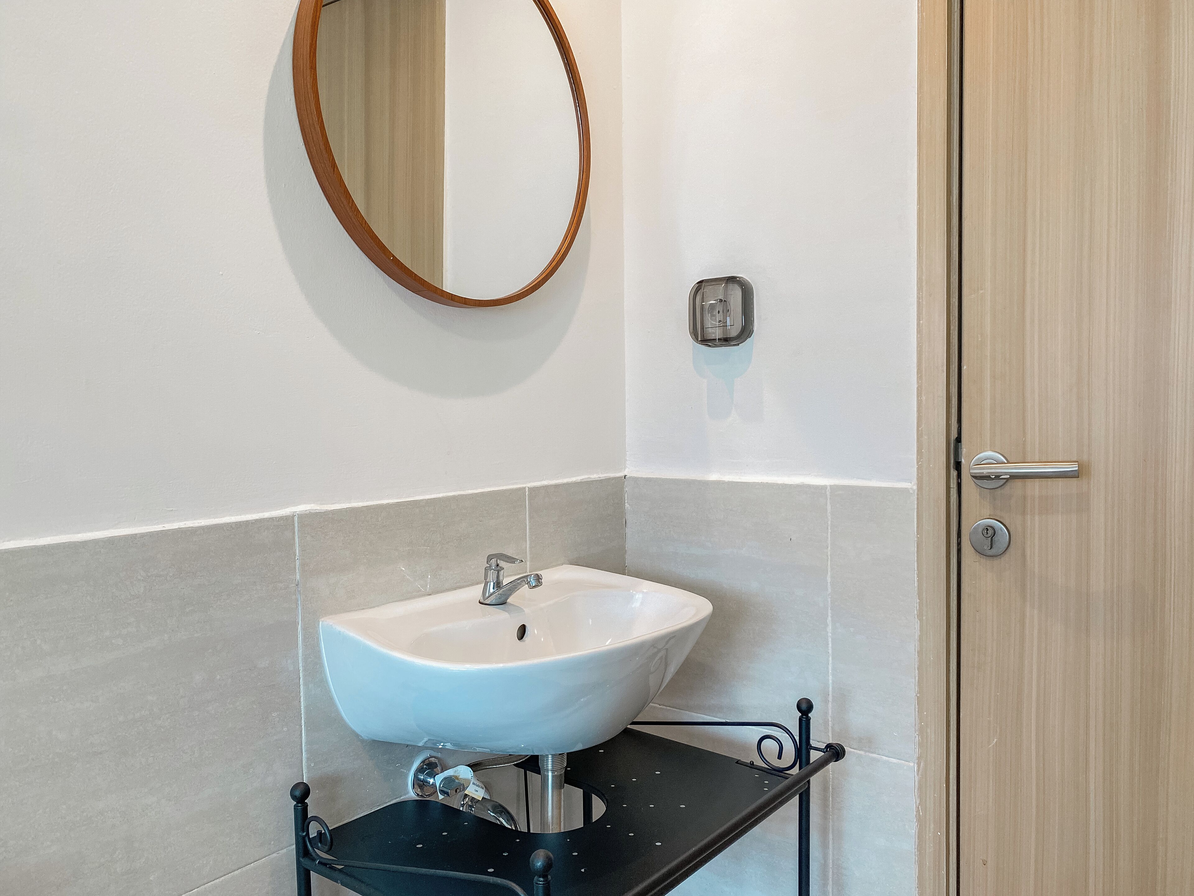 A bathroom with a white sink, a round mirror, and a wooden door.