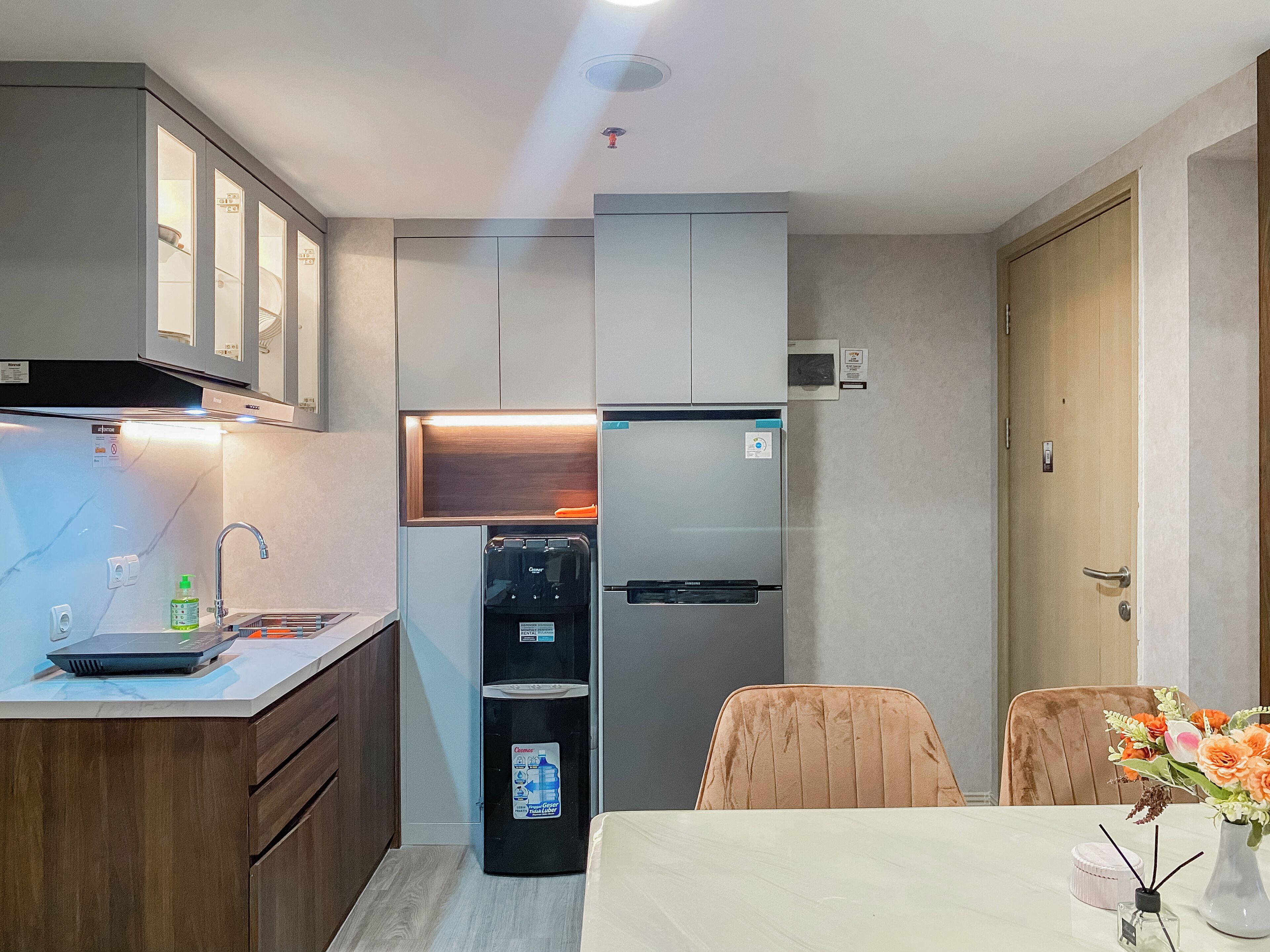 A compact kitchen with a refrigerator, water dispenser, and a sink. There is a dining area with a table and chairs.