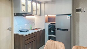 A compact kitchen with a built-in refrigerator, a sink, and wooden cabinets. - Homey And Modern Look 3Br At Meikarta With Balcon Apartment (Cikarang)