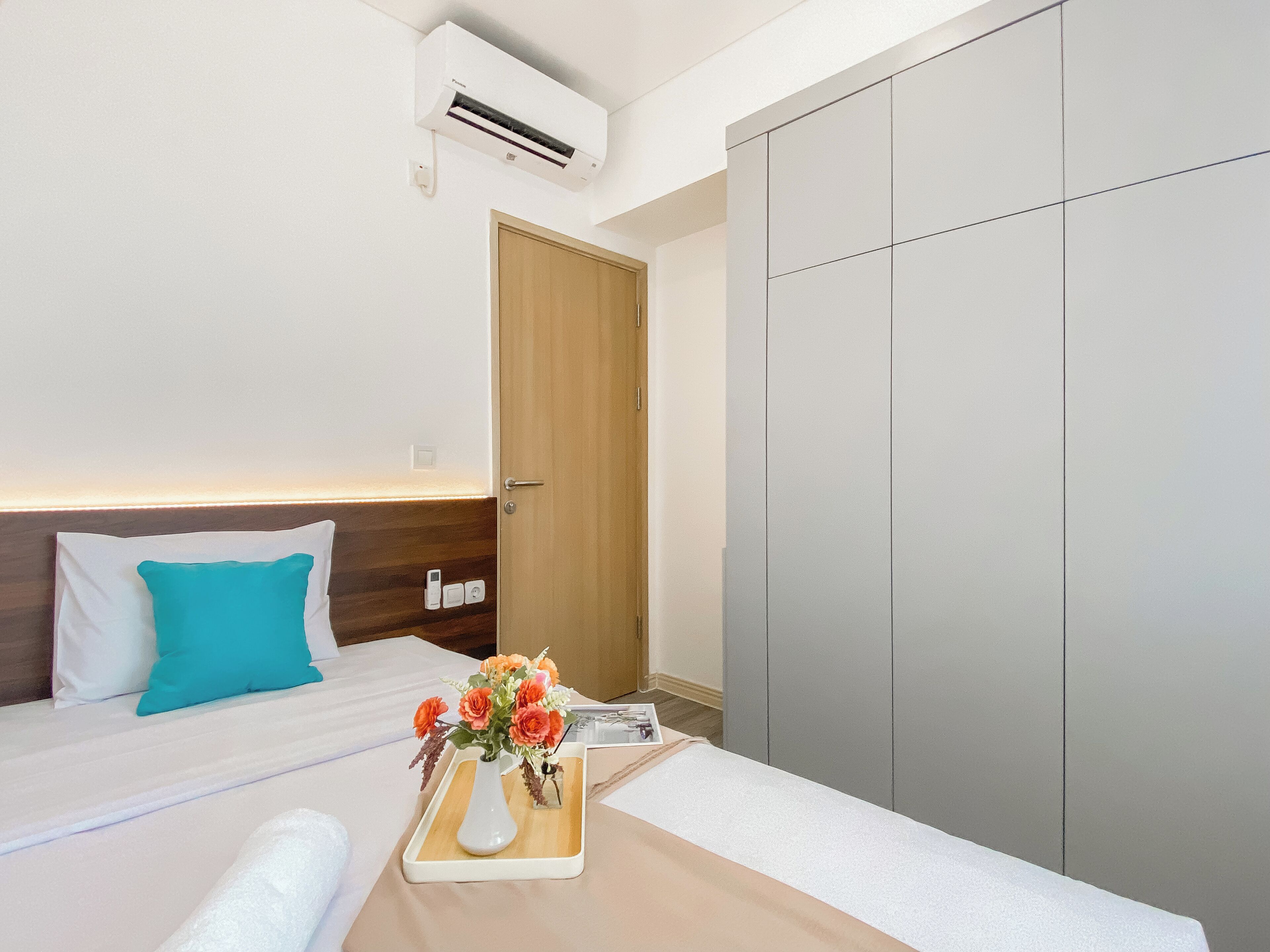 Habitación de hotel con cama, mesita de noche con un florero, armario y equipo de aire acondicionado.