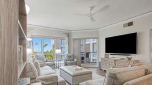 A spacious living room with a large TV, comfortable seating, and a balcony with a view. - 4203 Newly Renovated 1BR 2BA Direct Ocean/Beach Views Sofa Bed Soaking Tub (Hilton Head Island)
