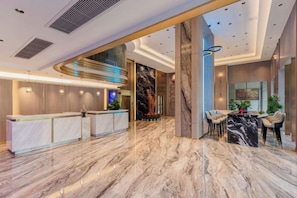 Una hall moderna di un hotel con pavimento in marmo, una reception, un'area salotto e un'ampia parete con una statua.