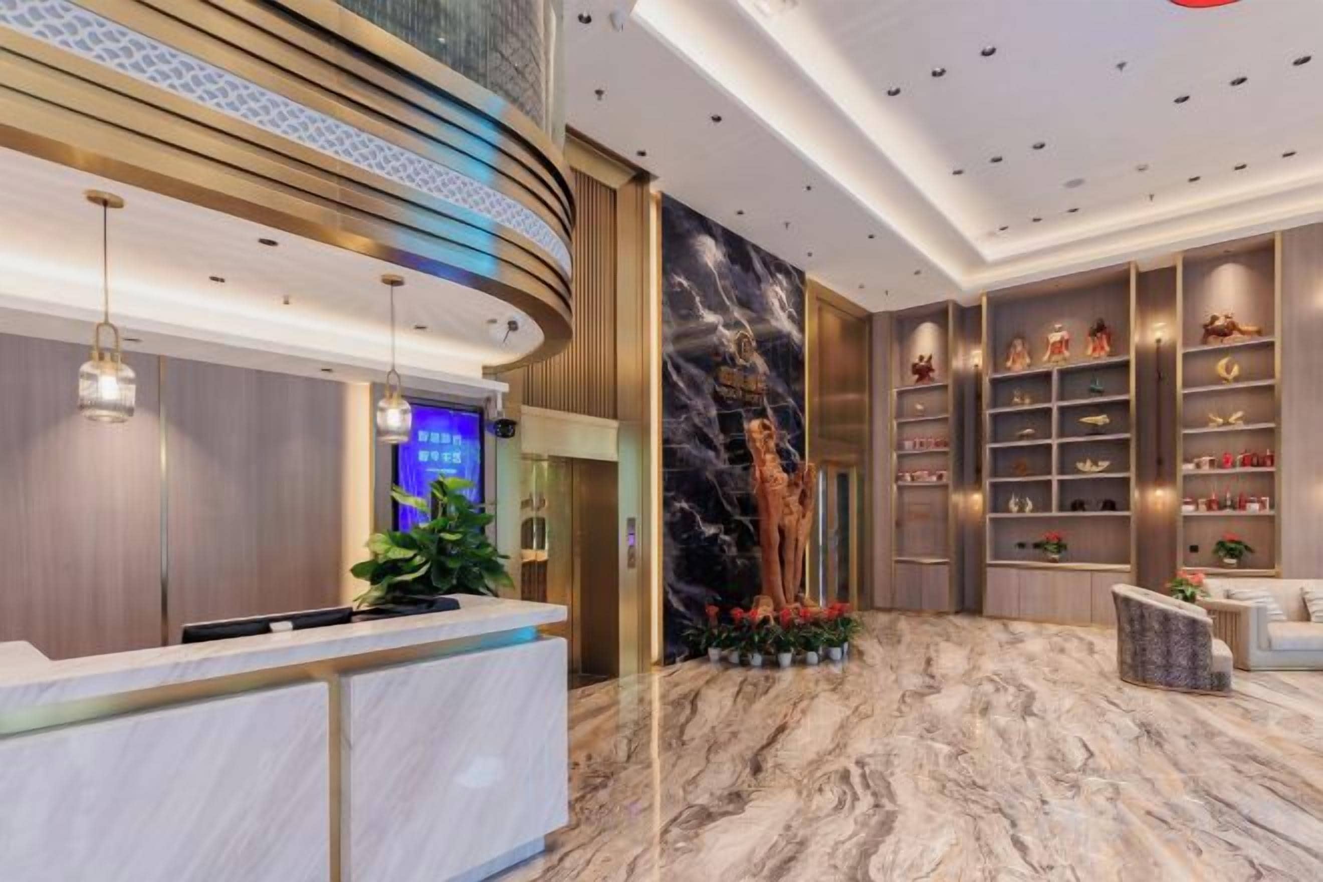 Zona de recepción de un hotel con suelo de mármol, mostrador de recepción y una pared con estanterías que exhiben diversos objetos.
