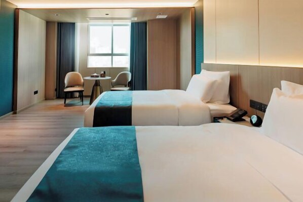 A hotel room with two beds, a small table, two chairs, a window, and a wall-mounted phone. - Bolin Hotel (Zhongshan)
