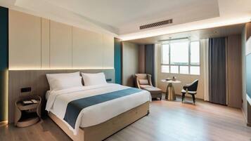 A modern hotel room with a large bed, bedside tables, a small desk, and a chair.