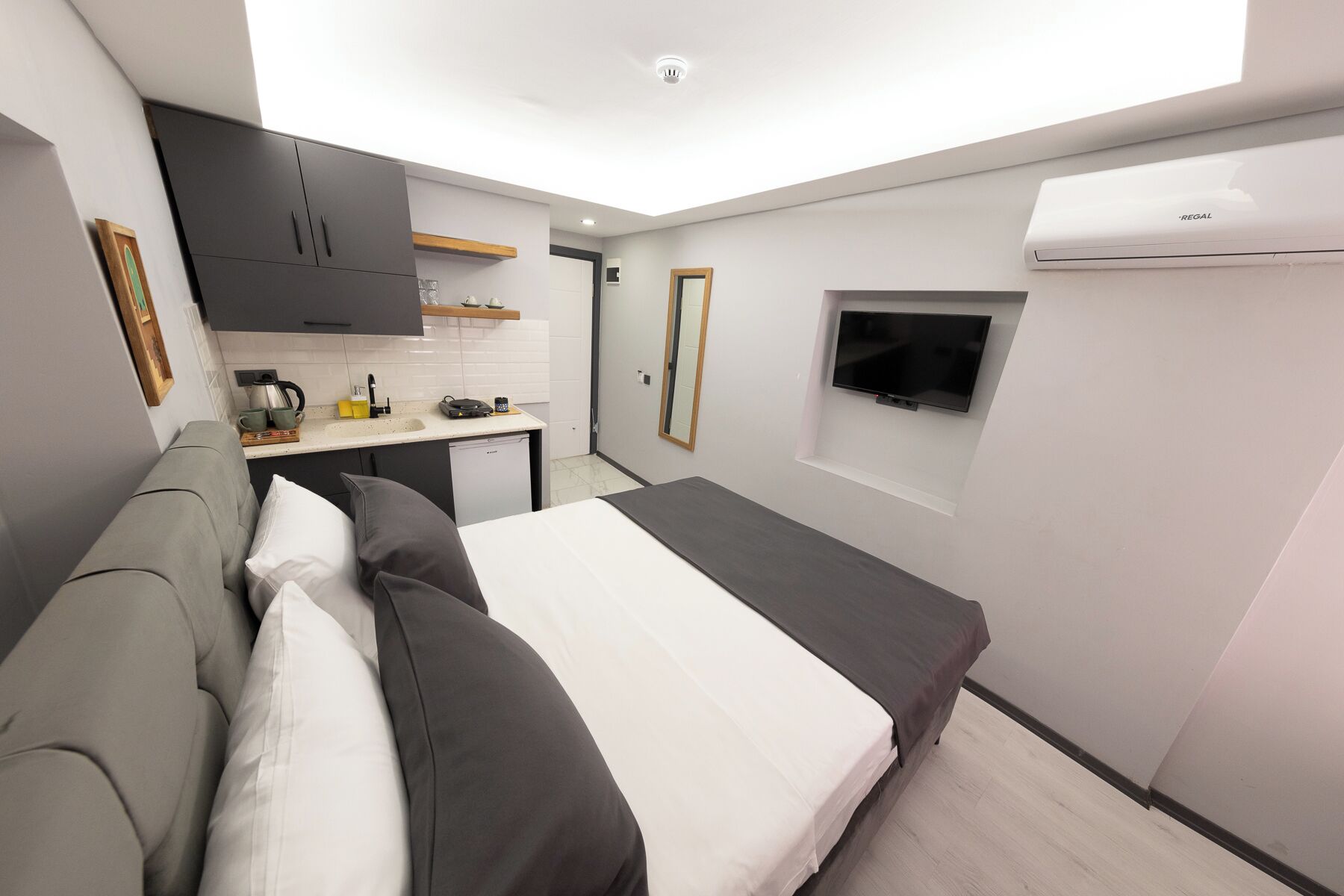 A compact room with a bed, a kitchenette, a TV, and an air conditioning unit.