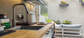 Cozinha moderna com pia de aço inoxidável, fogão embutido e janela com vista para um jardim.