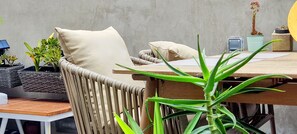 Uma cadeira de vime com almofadas, uma mesa de madeira e plantas em vasos.