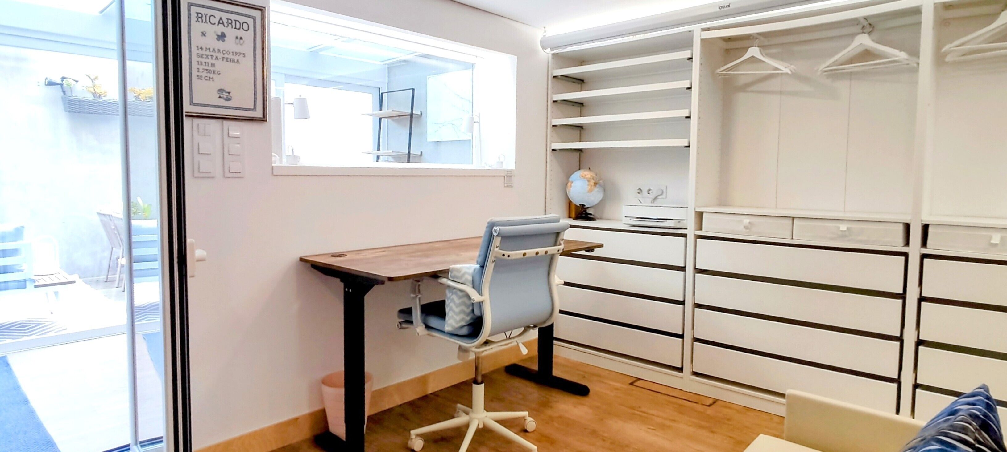 Ein Zimmer mit Schreibtisch, Stuhl und begehbarem Kleiderschrank mit mehreren Regalen und Kleiderbügeln.