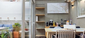 Uma cozinha moderna com painel de parede de mármore, um espaço de refeições com mesa e cadeiras, e vista para uma área externa com assentos através de uma porta de vidro.