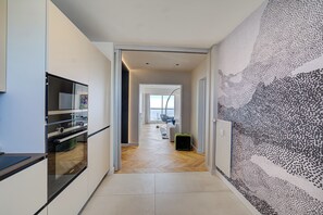 Enter a spacious living area with a sleek kitchen, abstract art, and a large window offering a view of the outdoors.