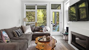 A living room with a gray sectional sofa, a wooden coffee table, a fireplace, and a TV mounted on the wall. - Beautiful & Modern Condo, Ski-In Ski-Out (Sun Peaks)