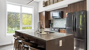A modern kitchen with a large island, stainless steel appliances, and a view of the outdoors. - Beautiful & Modern Condo, Ski-In Ski-Out (Sun Peaks)