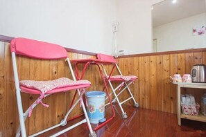 A room with wooden paneling, two pink chairs with white frames, a blue bucket, and a small shelf with items. - Jiufen Kaomama Hostel (New Taipei City)