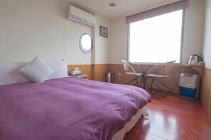 Ein Hotelzimmer mit Bett, einem kleinen Tisch, einem Stuhl, einem Fenster und einem Papierkorb.