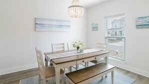 Un espace repas comprenant une table en bois, des chaises, un banc, un lustre et des œuvres d’art accrochées aux murs.