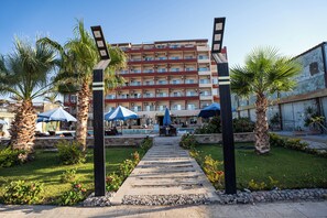Entrada d'hotel amb piscina, palmeres i un camí cap a l'edifici.