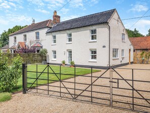A white house with a tiled roof, a gravel driveway, and a metal gate.