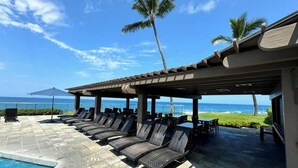 Un área junto a la piscina con sillones de descanso y una pérgola con vistas al océano.