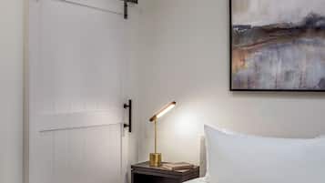 A neatly made bed with white bedding, a bedside table with a lamp, and a painting on the wall.