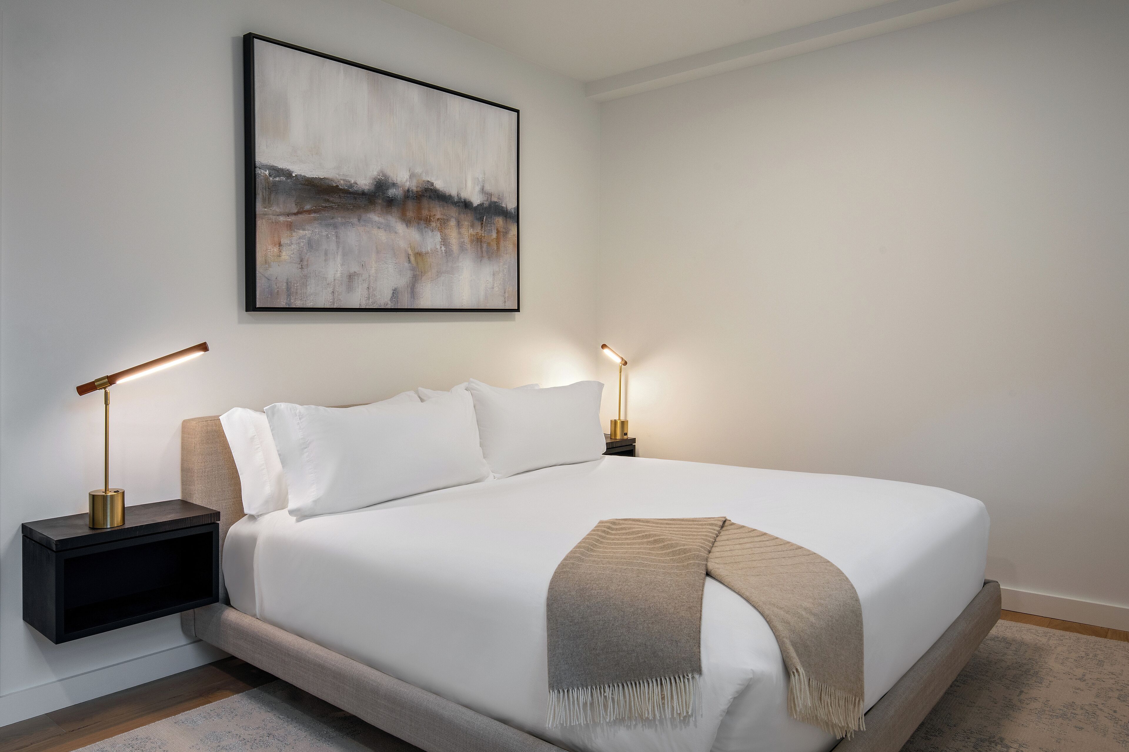 A neatly made bed with a white comforter and a beige throw blanket, flanked by two bedside tables with lamps.