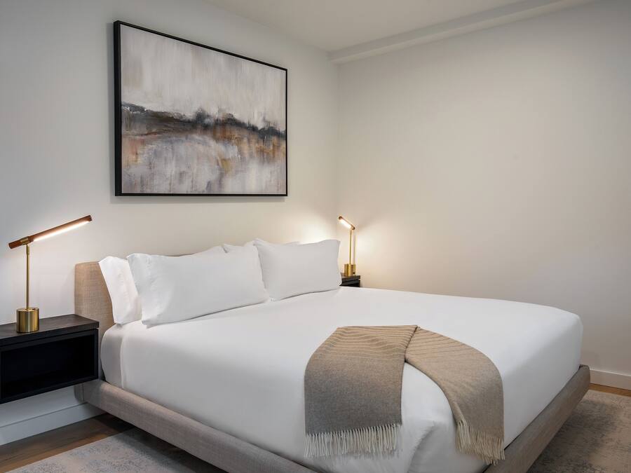 A neatly made bed with a white comforter and a beige throw blanket, flanked by two bedside tables with lamps.