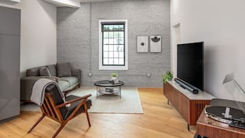 Un salon moderne comprenant un canapé, une chaise en bois, une table basse, un téléviseur et une platine vinyle.
