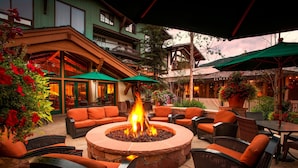 An outdoor seating area with a stone fire pit, wicker furniture, and green umbrellas.
