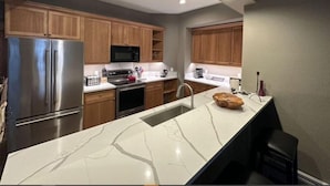 A modern kitchen with wooden cabinets, stainless steel appliances, and a marble countertop. - Spacious 2BR+Den Condo at Lodge Brookside (Avon)