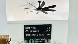 A kitchen with a wooden cabinet, a coffee machine, and a chalkboard menu listing prices for coffee, cold milk, and beignets.
